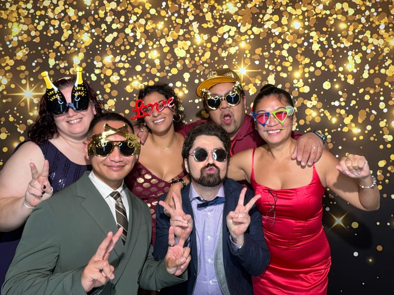 Wedding guests posing with props against a gold digital photo booth backdrop